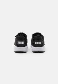 Baskets noires de sport avec des semelles blanches, dotées d'une cheville rembourrée, d'une languette et d'un logo Puma blanc bien visible au niveau du talon.