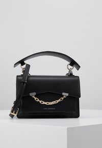 Borsa in pelle nera di Karl Lagerfeld con dettagli in catena dorata, manico superiore e tracolla regolabile su una superficie bianca.