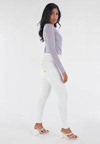 Haut à manches longues gris clair avec fronces, associé à des leggings blancs taille haute comportant des coutures accentuées et un petit logo.
