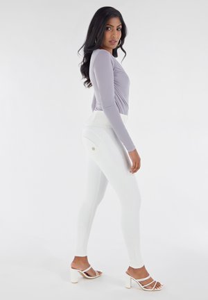 Haut à manches longues gris clair avec fronces, associé à des leggings blancs taille haute comportant des coutures accentuées et un petit logo.