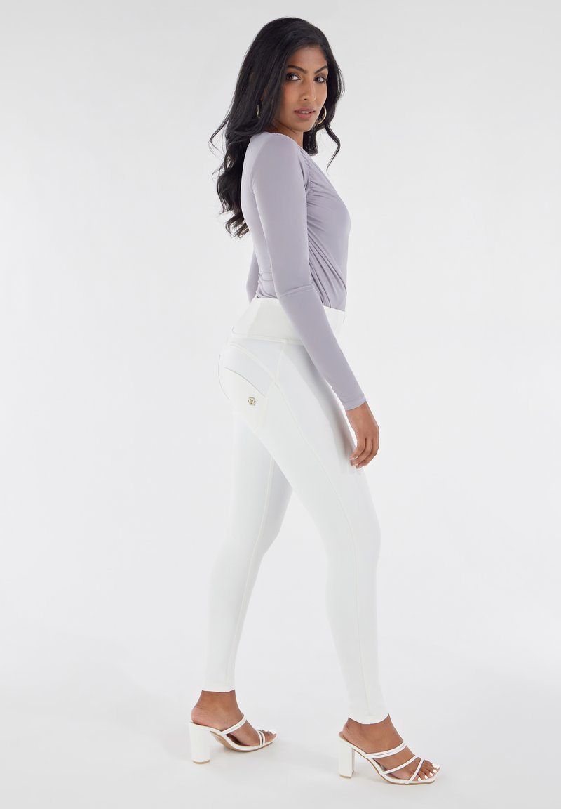 Haut à manches longues gris clair avec fronces, associé à des leggings blancs taille haute comportant des coutures accentuées et un petit logo.