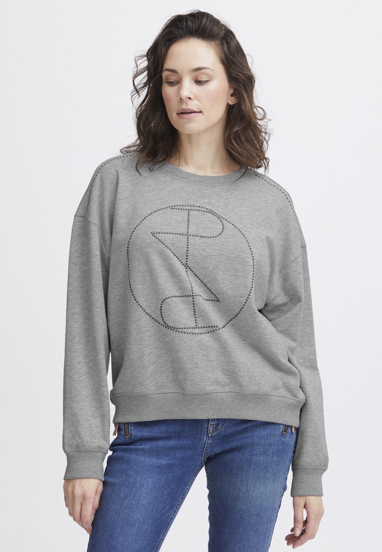 Sudadera gris con un patrón gráfico redondo delineado en pequeños studs, corte relajado, puños y dobladillo acanalados, combinada con jeans azules.