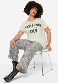 T-shirt bianca con il testo nero "YOU ♥ ME ♥ OUI", abbinata a pantaloni larghi a righe zebra bianchi e neri. Stivali neri con borchie alla caviglia.