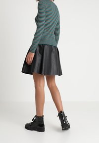 Striped, long-sleeve top in teal, black, and red, paired with a black faux leather flared skirt. Black lace-up ankle boots.