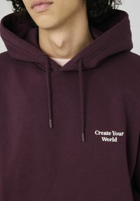 Sweat à capuche marron avec capuche à cordon de serrage et texte brodé en blanc "Create Your World" sur le devant. Tissu doux avec une coupe décontractée.