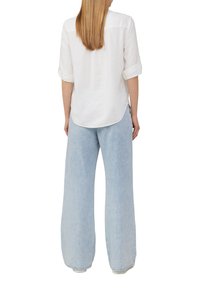 Chemise blanche à manches longues avec des poignets retroussés ; associée à un jean large bleu clair en denim doux. Vue arrière montrée.