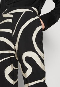 Zwarte stoffen broek met bold, witte abstracte golvende patronen, met een relaxte pasvorm en zijzakken. Gladde textuur met een hoge taille.