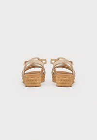 Sandali wedges beige con suola a strati, dotati di cinturini incrociati e una finitura texturizzata nella parte superiore.