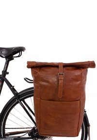 Sacoche en cuir marron à rabat enroulable, avec une poche avant et une sangle à boucle, fixée à un vélo noir. Texture lisse, design substantiel.