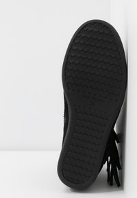 Černá semišová bota s texturovanou gumovou podrážkou, s třásněmi a velikostní štítkem 38 na spodní straně.