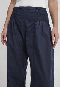 Pantalones de pierna ancha en azul marino con cintura fruncida, que presentan una textura suave y un ajuste holgado, diseñados para la comodidad y la transpirabilidad.