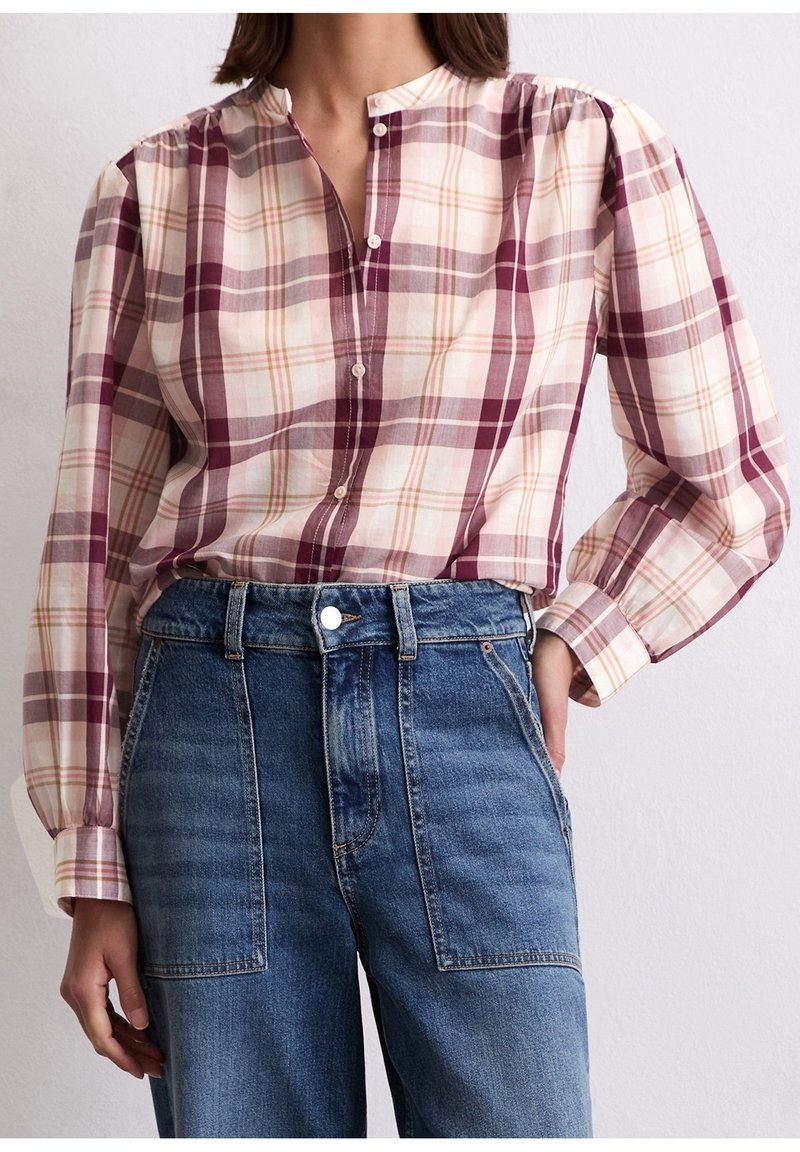 Femme portant une chemise à carreaux violette et crème à manches longues boutonnée, rentrée dans un jean en denim bleu taille haute.