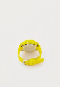 Kollane kummist randmekell, millel on ruudukujuline korpus, metallist seljaosa ning mustriline rihm. Omab hõbedast pandlat ja nähtavaid kruvistikandmeid.