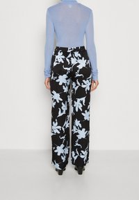 Jasnoniebieska bluzka z długim rękawem w połączeniu z czarnymi szerokimi spodniami w kwiaty, ozdobionymi jasnoniebieskimi i białymi wzorami kwiatowymi. Gładka tkanina, elastyczny pas.