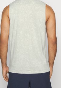 Chemise sans manches gris clair avec un motif texturé. Tissu doux, coupe décontractée et encolure ronde, avec un ourlet droit à la taille.