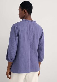 Camicia di cotone viola, con texture, dal collo arricciato e maniche a tre quarti. Vestibilità ampia, l'orlo scende sotto i fianchi. Design semplice.