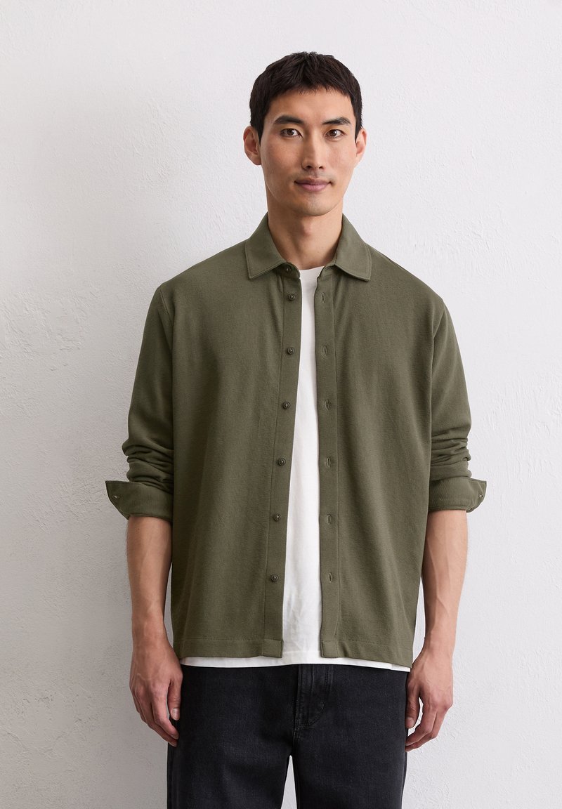 Camicia verde oliva con bottoni, colletto a punta, realizzata in tessuto morbido; presenta maniche arrotolate e delicati dettagli con bottoni. Stile casual.