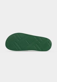 Semelle de sandale avec une bande de roulement en caoutchouc vert foncé présentant un motif géométrique de lignes et de rectangles qui se croisent, montrée sur un fond clair uni.
