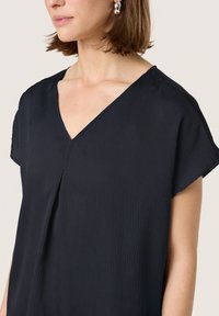 Blusa azul marino de corte holgado con escote en V, mangas cortas y tejido texturizado con sutiles líneas verticales.
