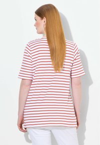 Pruhované tričko s červenými a bílými vodorovnými pruhy, krátkými rukávy a volným střihem. Tkanina vypadá hladce; lem na zadní straně je mírně delší.