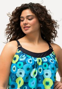 Färgglad lätt blus med ett blått och grönt cirkelmönster, svart halsringning och justerbara remmar. Mjuk, flödande tyg.