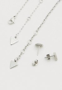 Σετ ασημένια κοσμήματα που περιλαμβάνει αλυσίδα κολιέ με τριγωνικά κρεμαστά και δύο ζευγάρια σκουλαρίκια καρφάκια, το ένα με κρύσταλλα.