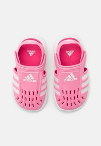 Par de sandalias Adidas rosas de tipo slip-on con franjas blancas y agujeros de ventilación, vistas desde arriba sobre un fondo blanco.