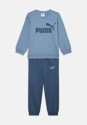 Jasnoniebieska bluza z ciemnoniebieskim logo "PUMA", zestawiona z dopasowanymi niebieskimi spodniami dresowymi z logo na nodze. Oba elementy mają ściągacze.