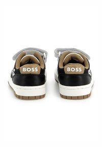 Sneaker bianco e nero con accenti marroni, forma arrotondata, materiali in pelle e tessuto lisci, dotato di una fascetta in velcro e dettaglio del logo.