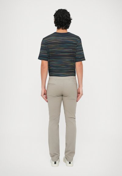 Koszula w krótkim rękawie w wielokolorowe paski, zestawiona z jasnobeżowymi spodniami i białymi butami; uwaga skupiona na poziomych liniach koszuli i jej dopasowaniu.