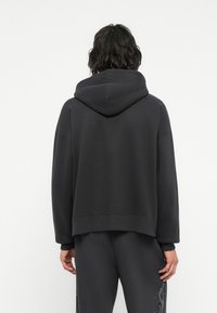 Felpa con cappuccio grigio scuro, con polsini e orlo a coste. Presenta una vestibilità rilassata e un tessuto testurizzato. Dettaglio di cucitura discreto sul retro.