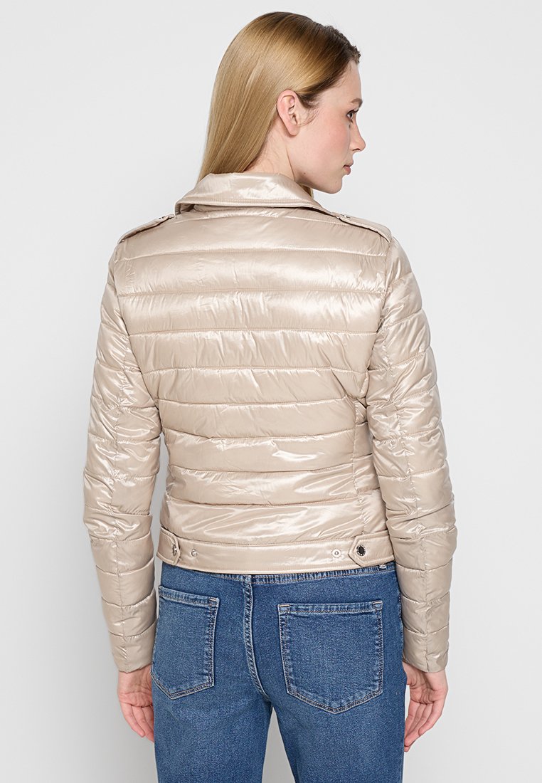 Beige Daunenjacke mit glänzender, gesteppten Finish, ausgestattet mit einem Kragen und seitlichen Druckknöpfen. Getragen mit blauen Jeans. Rückansicht dargestellt.