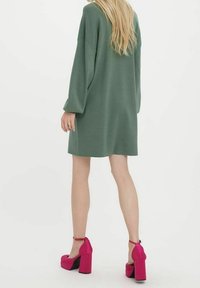 Robe-pull surdimensionnée à manches longues de couleur verte pâle, avec une coupe décontractée. Associée à des talons compensés rose vif avec brides à la cheville.