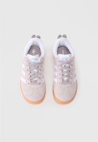Bež športni copati Adidas z belimi črtami, gumijastimi podplati, sivimi vezalkami, jezikom s temami Disneya ter mehkim belim krznom in sivimi petnimi vložki.