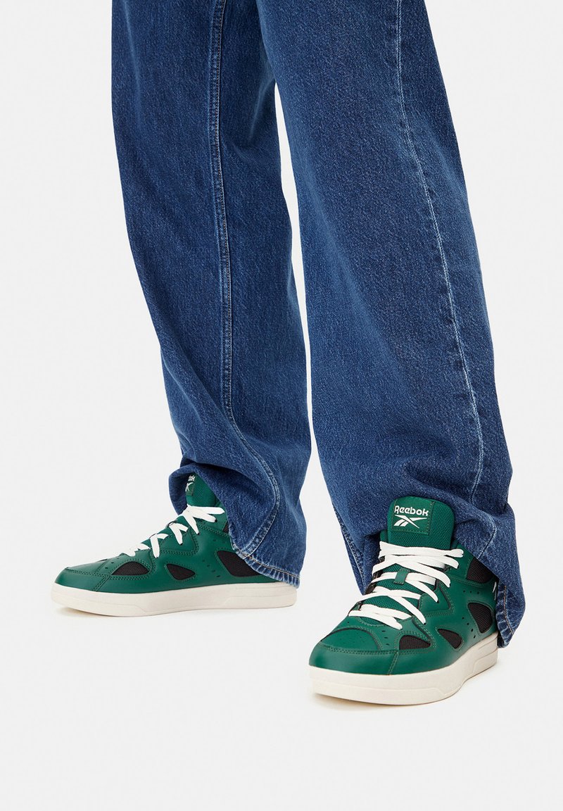 Grüne High-Top-Sneaker mit weißen Schnürsenkeln und schwarzen Akzenten, aus Leder und Mesh, kombiniert mit lockeren blauen Jeans.