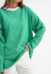 Groene en witte gestreepte langarmshirt met een roze geribbelde kraag en een losse pasvorm. Bevat logo aan de voorkant en een casual stijl.