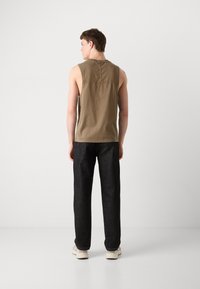 Khaki ermeløs skjorte med rund hals, kombinert med mørke denimbukser. Antrekket fullføres med lyse joggesko.