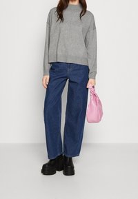 Sweater cropped gris, jeans en denim bleu à jambes larges, bottes à plateforme noires et un sac rose avec une poignée nouée. Textures lisses et design moderne.