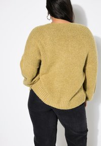 Pletený svetr v světle žluté barvě, s uvolněným střihem, žebrovaným lemem a širokými rukávy. V kombinaci s tmavými, strukturovanými kalhotami.