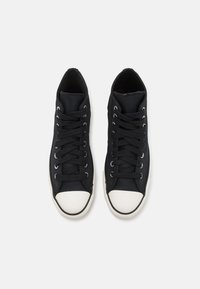Zapatillas de lona negras con una puntera de goma blanca, cordones planos y un upper texturizado. Diseñadas con un perfil bajo y un collar acolchado.