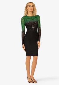 Zwarte bodycon jurk met lange groene en zwarte gestipte mesh mouwen. Beschikt over een aansluitende silhouette met een ronde halslijn en een soepele textuur.