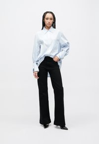 Niebieska koszula w paski z kołnierzykiem zapinanym na guziki i kieszenią na piersi, zestawiona z dopasowanymi czarnymi spodniami i czarnymi szpilkami z szpiczastymi noskami.