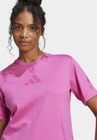 Růžové sportovní tričko s krátkým rukávem vyrobené z hladké tkaniny, s decentním designem loga a minimalistickými detaily na rukávech.