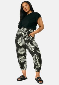 Haut noir à manches courtes associé à un pantalon noir et blanc à motif de feuilles de palmier, doté de poches latérales et d'un ourlet fuselé. Porté avec des sandales noires.