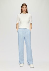 Lichtgewicht witte top met korte mouwen, gecombineerd met blauw gestreepte broek. De broek heeft een elastische tailleband en een ontspannen pasvorm. Witte sneakers.