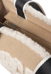 Interno della borsa beige con fodera soffice bianca, cerniera dorata e cinghie nere. Presenta un logo sul cursore della cerniera e bordi a contrasto.