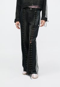 Μαύρο τζιν με δαντελωτό σχέδιο στο πλάι, με ασημένιες τρύπες για κορδόνια. Συνδυάζεται με κοντό μαύρο μπουφάν και ανοιχτό ροζ παπούτσια. Λευκές ρίγες στα πλάγια.