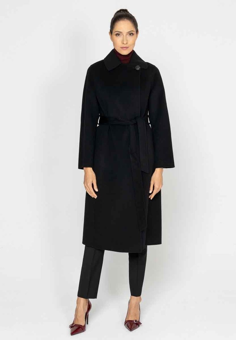 Czarny wełniany płaszcz trench z wysokim kołnierzem, zapinany na wiazanie, z paskiem w talii. Połączony z czarnymi eleganckimi spodniami i błyszczącymi burgundowymi szpilkami.
