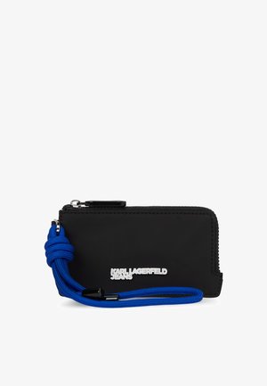 Melna zip somiņa ar zilu pīts siksniņu, ar gludu tekstūru un sudraba logotipu. Kompakta taisnstūra forma, ērti pārnēsājama.