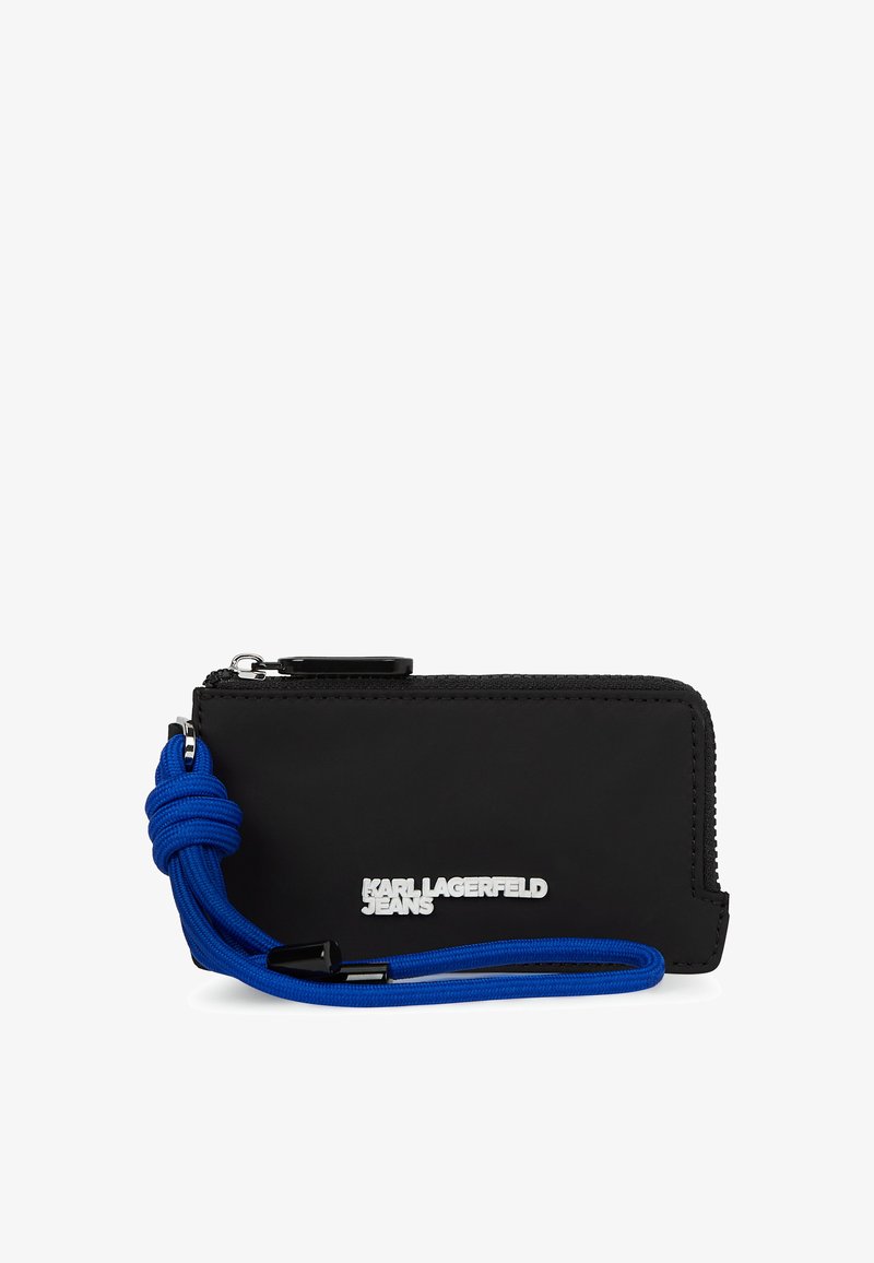 Melna zip somiņa ar zilu pīts siksniņu, ar gludu tekstūru un sudraba logotipu. Kompakta taisnstūra forma, ērti pārnēsājama.